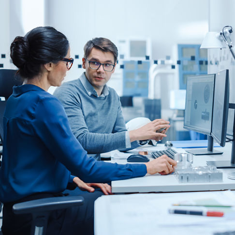 Modern Factory: Male Industrial Engineer Explains to Female Project Supervisor Functions of the Machine Part Comparing it to one on Computer Screen. They use CAD Software for Design, Development